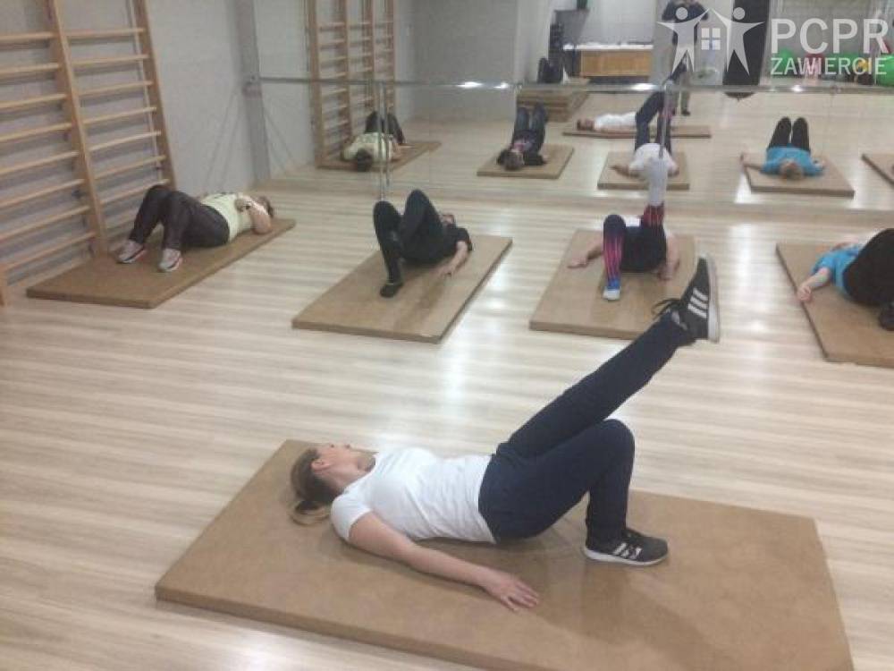 Zdjęcie: Grupa kobiet wykonuje ćwiczenia w sali gimnastycznej leżąc na plecach na macie